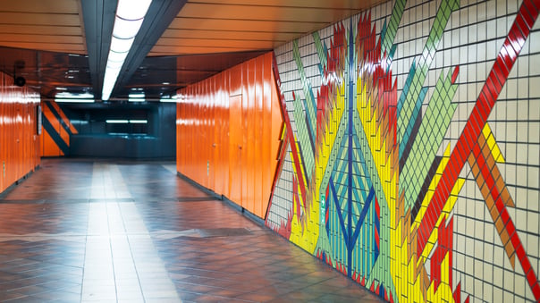 Colourful tiled wall graphics mural in an underground station corridor with patterned flooring and modern lighting. 