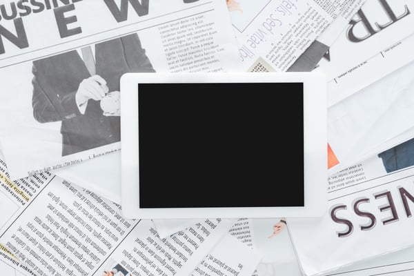 A digital tablet placed on top of spread out newspapers, representing the comparison between print and digital advertising for small businesses.