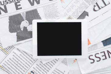 A digital tablet placed on top of spread out newspapers, representing the comparison between print and digital advertising for small businesses.