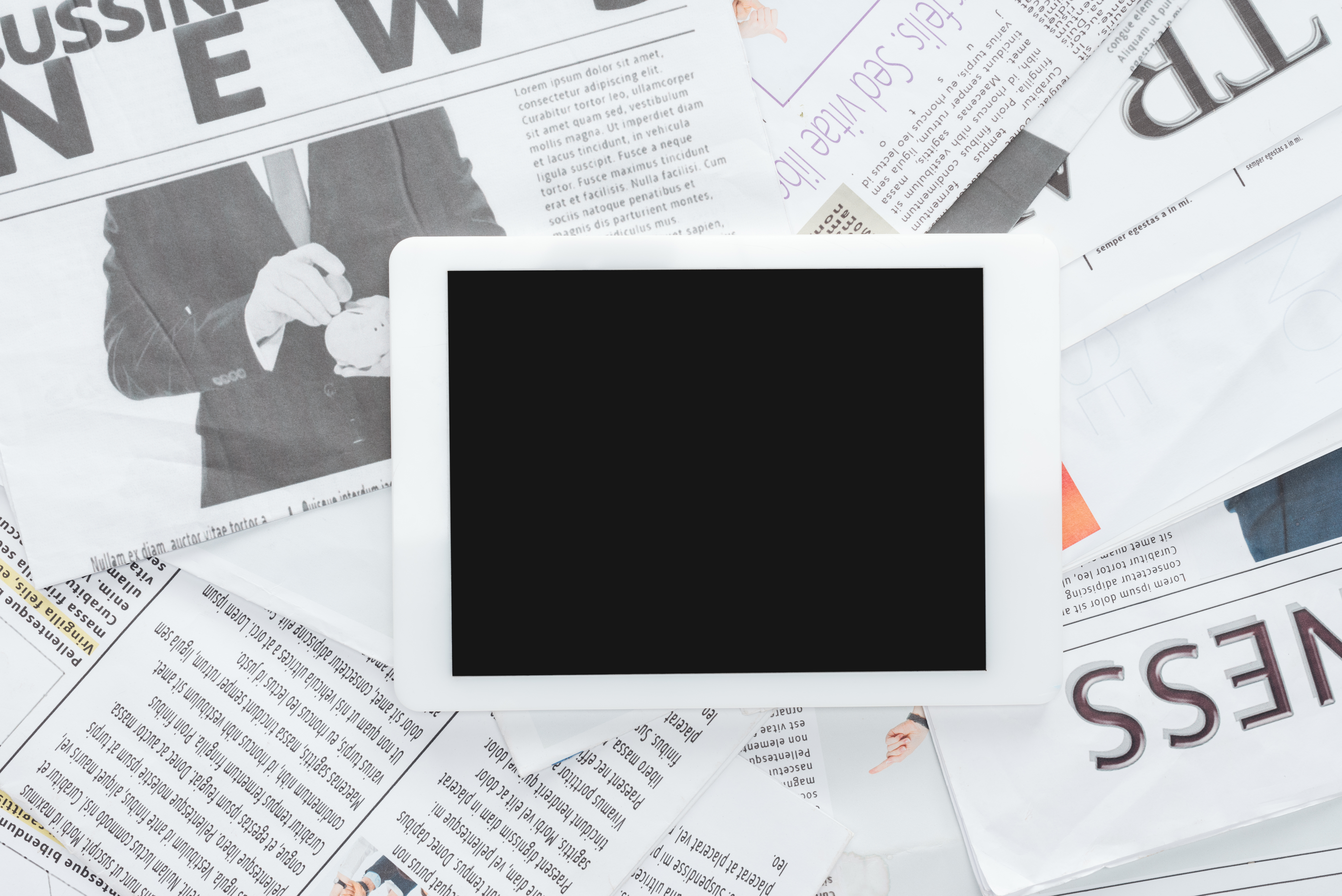A digital tablet placed on top of spread out newspapers, representing the comparison between print and digital advertising for small businesses.